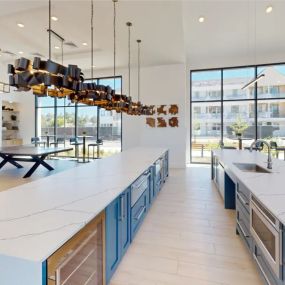 The spacious resident demo kitchen with blue cabinets, sleek appliances, long countertops, and pendant lighting