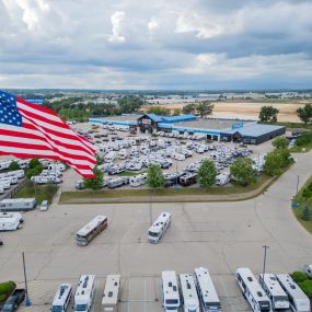 aerial view of Camping World in Madison, WI showing the building and many RVs in front of it, the sky and many trees and a Camping World sign and large American flag