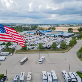 aerial view of Camping World in Madison, WI showing the building and many RVs in front of it, the sky and many trees and a Camping World sign and large American flag