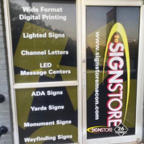 Window display of Signstore listing services: Wide Format Digital Printing, Lighted Signs, Channel Letters, LED Message Centers, ADA Signs, Yards Signs, Monument Signs, and Wayfinding Signs. Signstore logo and 