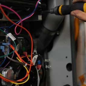 A picture of a panel open with exposed wires and a hand holding a screwdriver to repair something