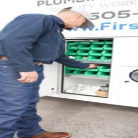A picture of a man in front of a work truck with the side storage compartment open looking for a part