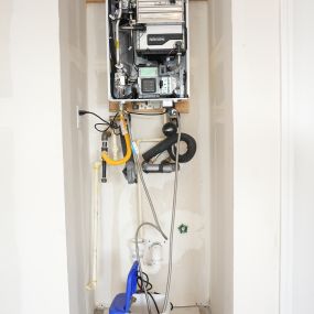 A picture of a tankless water heater mounted on a wall with the cover taken off and everything on the inside exposed