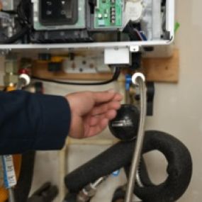 A picture of a water heater with the cover removed and a  hand adjusting something on the bottom