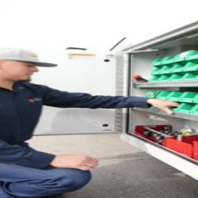 A picture of a man in front of a work truck with the side storage compartment open selecting a part