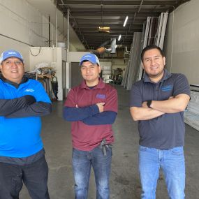 A picture of the crew at Unlimited Garage Door Services standing in their building with panels for garage doors behind them