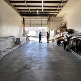 A picture of Unlimited Garage Door Services space looking from inside the building to the outside with the garage door open and workers standing by the door