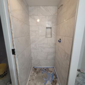 A picture of a tile shower with an unfinished floor and no fixtures