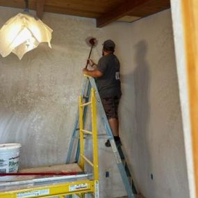 A picture of a man standing on a ladder sanding a wall