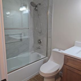 A picture of a bathroom with a toilet, vanity, tub with glass doors, and new fixtures, and tile floor