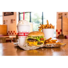 A Five Guys cheeseburger, milkshake and regular order of fries sits on a table inside a Five Guys restaurant.