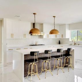 Bright and spacious modern addiction treatment center kitchen featuring a large island with gold fixtures, seamlessly connecting to an open living area with floor-to-ceiling windows.