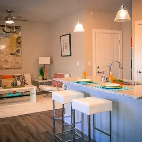A kitchen with an island and stools in front of a living room with a couch