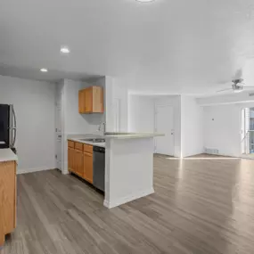 View of expansive living room and kitchen area with plank flooring, natural light, and a sliding glass dooes that lead to a patio or balcony