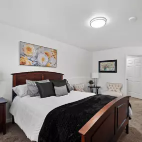 Bedroom with plush carpeting, bed, nightstand with lamp, and view into bathroom vanity