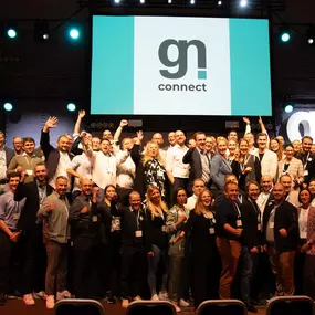 Eine große Gruppe von Menschen steht auf einer Bühne vor einer Leinwand mit dem Logo von „gn connect“. Es handelt sich um eine Veranstaltung, bei der eine Gemeinschaft aus der Gastronomie- und Digitalisierungsbranche zusammenkommt, im Rahmen gastronovi-Events gn connect in Bremen in der alten Werft.