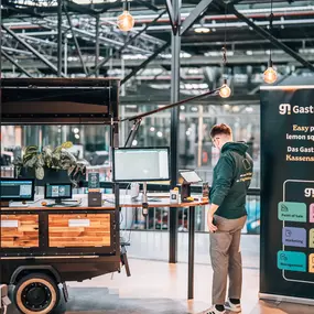 Gastronovi Messestand: Mitarbeiter präsentiert live das intuitive Kassensystem im Foodtruck-Look. Banner zeigt das Komplettsystem für moderne Gastronomie.