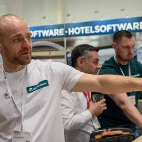 Gastronovi Messestand: Mitarbeiter in weißem Shirt erklärt die Software live am Bildschirm. Besucher verfolgen die Demo der Gastro-Software. Banner im Hintergrund sichtbar.