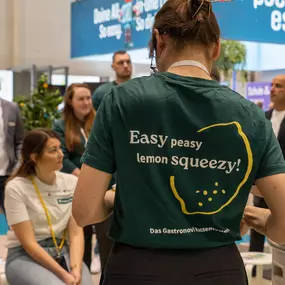 Gastronovi-Mitarbeiterin trägt ein T-Shirt mit dem Spruch „Easy peasy lemon squeezy!“ – und kommt damit humorvoll ins Gespräch mit Messebesuchern. Ein sympathischer Auftritt, der zeigt: Digitalisierung darf auch Spaß machen.