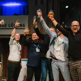 Jubelnde Stimmung auf der gn connect! Eine Gruppe stößt mit Gläsern an und feiert. Erfolg und positive Energie sind auf der Veranstaltung spürbar.