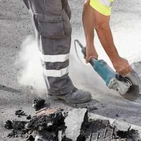 Worker using a power saw to cut through asphalt on a road