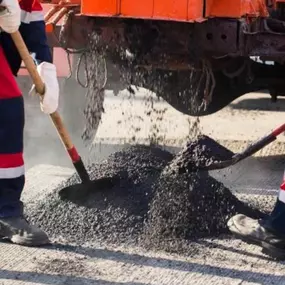 Workers scooping fresh asphalt with a pair of shovels