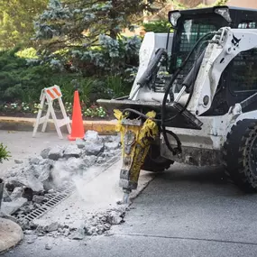 Dominion Paving Contractor drilling old concrete with a Bobcat