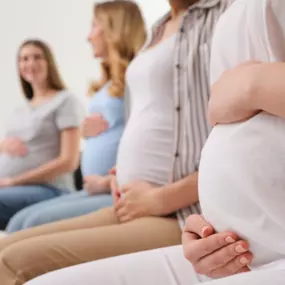 Das Bild zeigt vier schwangere Frauen, die entspannt nebeneinandersitzen und ihre Babybäuche halten. Diese Szene repräsentiert die Geburtsvorbereitungskurse bei Mamagold Stuttgart, die werdende Mütter umfassend auf die Geburt vorbereiten. In diesen Kursen vermitteln Isabel und Vanessa – erfahrene Hebammen und Pilates-Trainerinnen – wertvolles Wissen zur körperlichen Geburtsvorbereitung, Atemtechniken und Entspannungsübungen. Das Ziel: Frauen bestmöglich auf die Geburt und die erste Zeit mit ihre