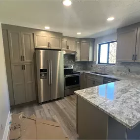 This newly remodeled kitchen features a bright, modern design with white and gray quartz countertops, custom shaker-style kitchen cabinets, and sleek stainless steel appliances. The neutral color palette adds timeless appeal while maximizing light and space in the room.