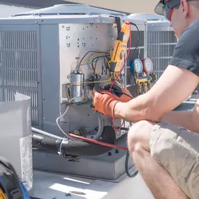 An HVAC technician is working on an air conditioning unit on a rooftop. He is wearing safety glasses and gloves, and is using tools to make adjustments to the unit. The unit is large and gray, with visible wires and pipes.