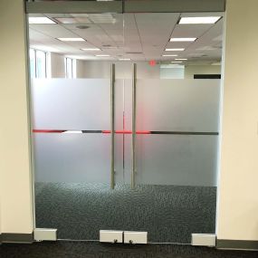 This image showcases a sleek installation of frosted window film by Precision Safety Films, PSF Window Tinting, at a dealership in Tampa, Florida.  The double horizontal opaque frost stripe design ensures privacy and style for the office within.