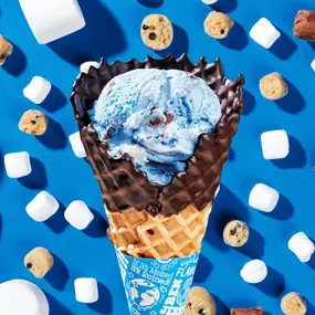 Marshmallow Sky ice cream in a chocolate dipped waffle cone on a blue background with marshmallows and cookie dough chunks.