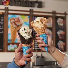 Dulce De-Lish! and Turtle Sundae in Waffle Cones at a Ben & Jerry's ice cream shop. Dulce De-Lish! is Salted Caramel Ice Cream with Pecan Toffee Pieces & Caramel Swirls. Turtle Sundae is Buttery Ice Cream with Fudge-Covered Almonds & Pretzel Swirls.