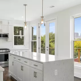 This kitchen features waterfall granite countertops and all-white fixtures, blending style and functionality. The large doors open up to breathtaking views of Midtown Atlanta, filling the space with natural light.