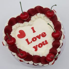 Heart cake with white frosting, decorated with red and white frosting borders, and topped with cherries. The cake features the message 