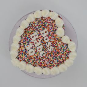 A vibrant heart-shaped cake covered in colorful sprinkles with the message 