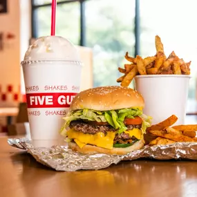 A Five Guys cheeseburger, milkshake and regular order of fries sits on a table inside a Five Guys restaurant.