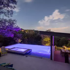 Infinity edge pool at night with LED color-changing lights and sunken outdoor kitchen area with fireplace and custom shade structure