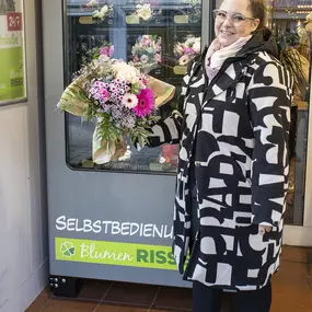 Frau steht mit gekauftem Blumenstrauß aus dem Blumen-Risse Blumenautomat in Dortmund-Mengede