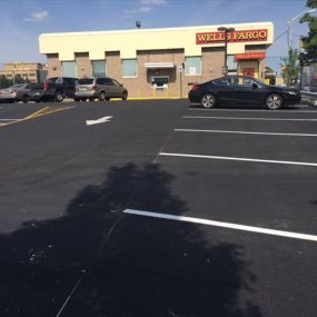 A newly paved parking lot with clear white lines and directional arrows in front of a Wells Fargo bank.