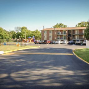 A freshly paved parking lot in front of a brick apartment building with cars parked along the side.