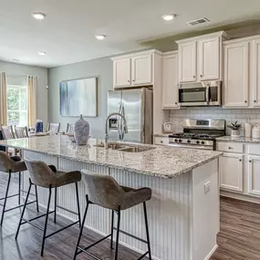 Kitchen with white cabinets and island with 3 bar stools in the DRB Homes Traditions at Crystal Lake community