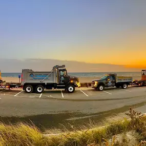 Shore Things Environmental fleet of trucks at a beach parked in parking lot with ocean in background and sun setting