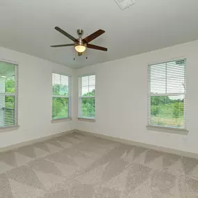 an empty living room with a ceiling fan and three windows