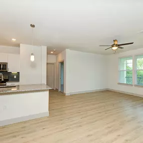 an empty living room with a kitchen and a ceiling fan