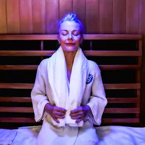 A woman wearing a rob relaxing during infrared sauna treatment