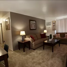Carpeted living room with cozy furnishings and warm lighting at Country Meadows Apartments in Ypsilanti, MI.