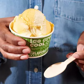 Person holding Mango ice cream in a cup at a Ben & Jerry's ice cream shop. Mango is Mango Ice Cream Swirled with Sweet Cream Ice Cream.