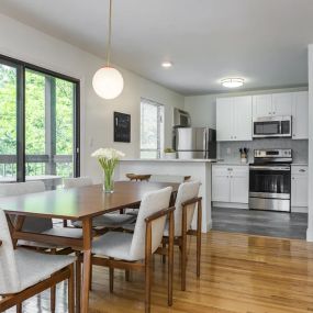 A dining room near a double sliding door to a patio with access to a kitchen with hardwood-style flooring and stainless steel appliances.