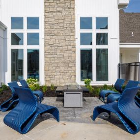 a patio with blue chairs and a fire pit in front of a building